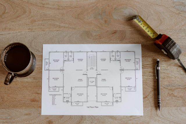 L'aménageur de bureau, ou space planner : rôle et apport Plan d'aménagement imprimé, mètre ruban, stylo et tasse sur une table en bois