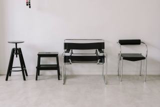 Chaises et tabourets de styles différents, dont des chaises à piètement luge, contre un mur blanc