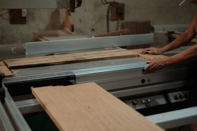 Comprendre la fabrication d'un meuble de bureau avant de choisir son fabricant Mains qui guident un panneau de bois sur une scie à format en atelier