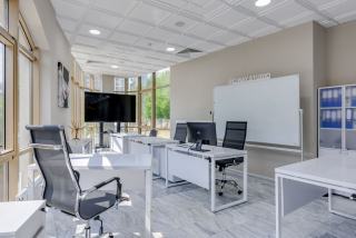 Bureaux blancs, sièges résille, écran mural et tableau blanc dans un local lumineux