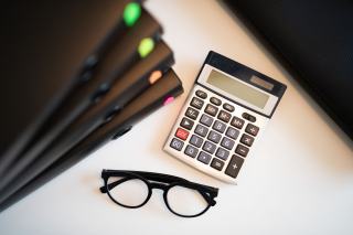 Calculatrice, lunettes et dossiers posés sur un bureau blanc